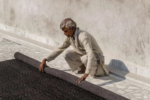 Man carefully unrolling a black patterned rug on tiled floor, demonstrating caring for your rug tips