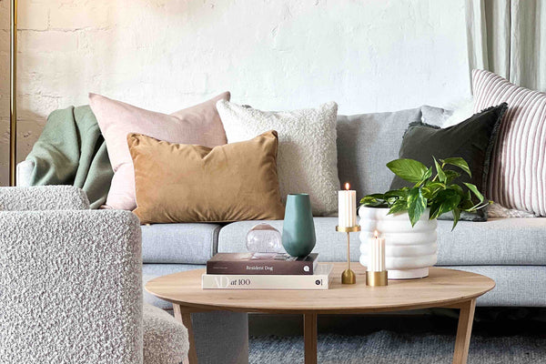 Cozy modern living room with soft textured sofa, warm cushions, wooden coffee table, indoor plants, and abstract wall art.