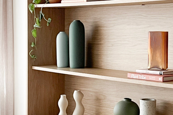 Minimalist wooden shelf styled with modern vases, books, and a trailing plant to style the perfect shelf