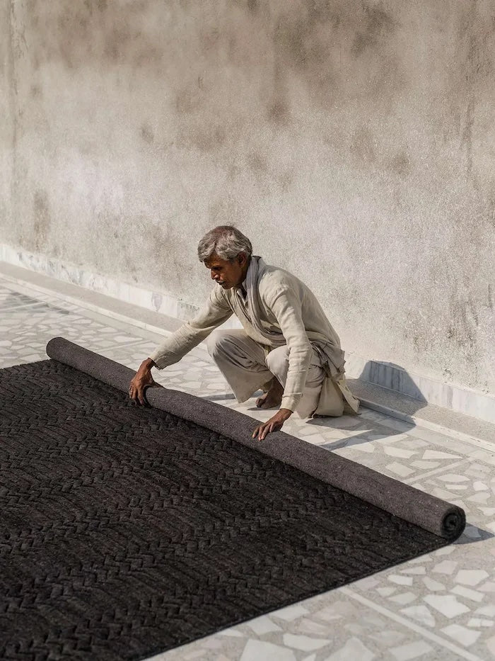 Man carefully unrolling a black patterned rug on tiled floor, demonstrating caring for your rug tips