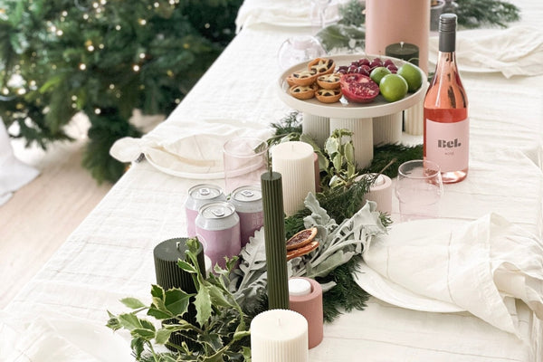 Festive holiday table setting with blush linen, greenery, candles, and rosé wine by a decorated Christmas tree