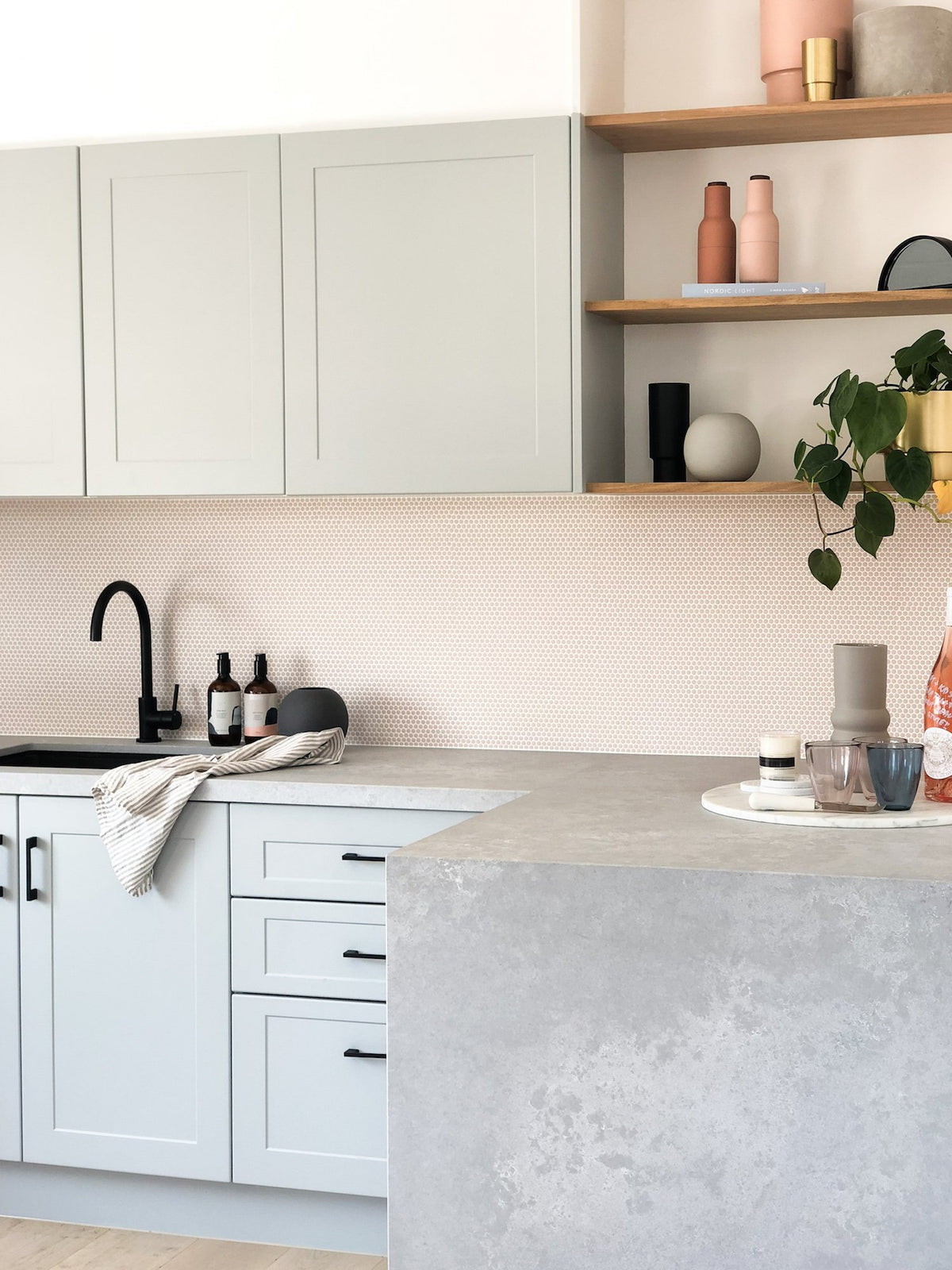 Modern kitchen with soft pastel cabinetry, blush glass tile backsplash, black matte fixtures, and open wooden shelves at norsuHOME concept store