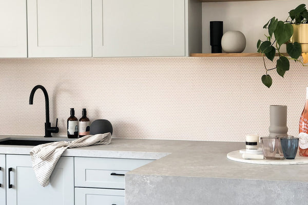 Modern kitchen with soft pastel cabinetry, blush glass tile backsplash, black matte fixtures, and open wooden shelves at norsuHOME concept store