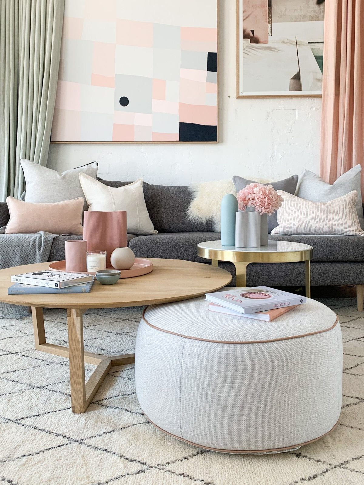 Modern living room with a round beige ottoman, wooden coffee table, gray sofa, and pastel decor accents