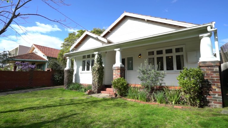 Front view of a renovated 1920s Californian bungalow with white exterior, brick columns, and a green lawn, representing norsuHOME - The Backstory.