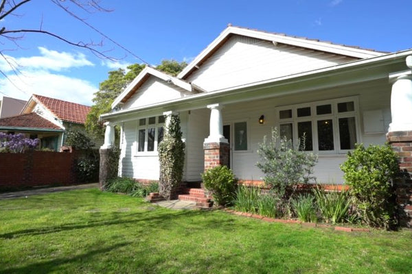 Front view of a renovated 1920s Californian bungalow with white exterior, brick columns, and a green lawn, representing norsuHOME - The Backstory.
