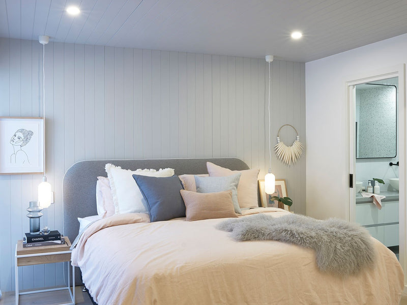 Cozy adults only retreat bedroom with soft pastel linens, textured accents, and modern ensuite visible through open door