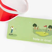 Open Golf Baby board book showing a golfer and hole in one illustration next to a red and white visor for toddlers