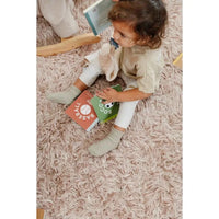 baby sitting on carpet holding Baseball Baby board book and plush toy