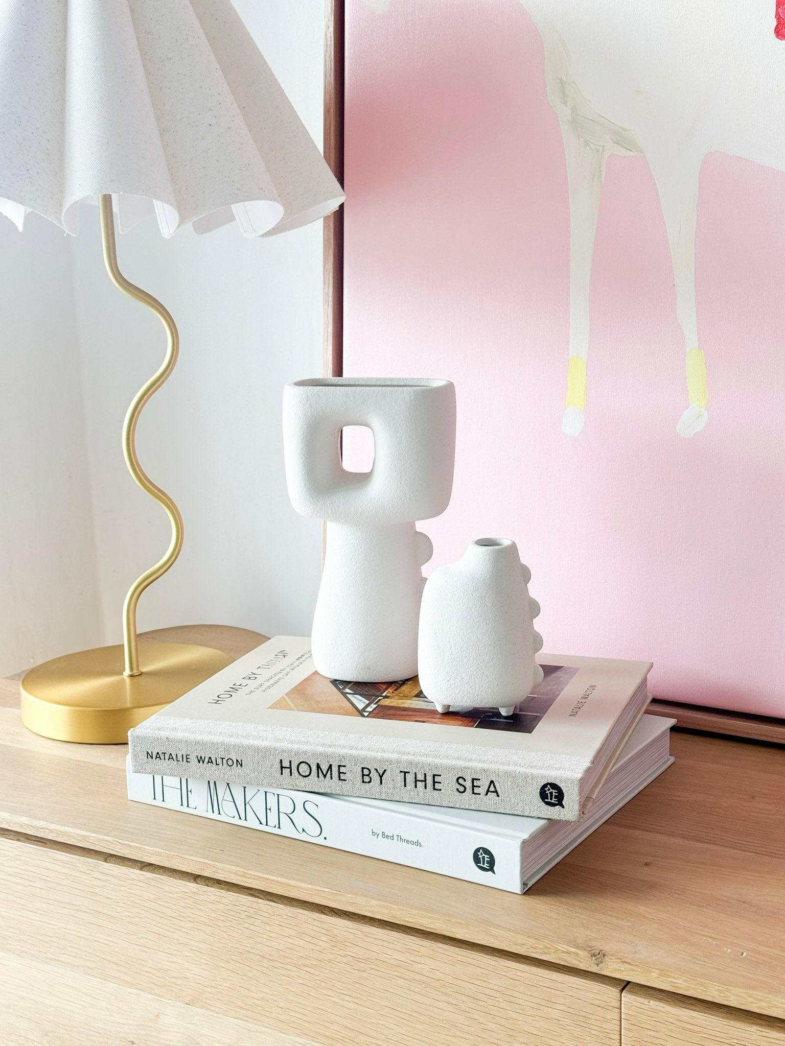 White Elle Vase ceramic with modern design displayed on books beside a gold lamp and pink wall art