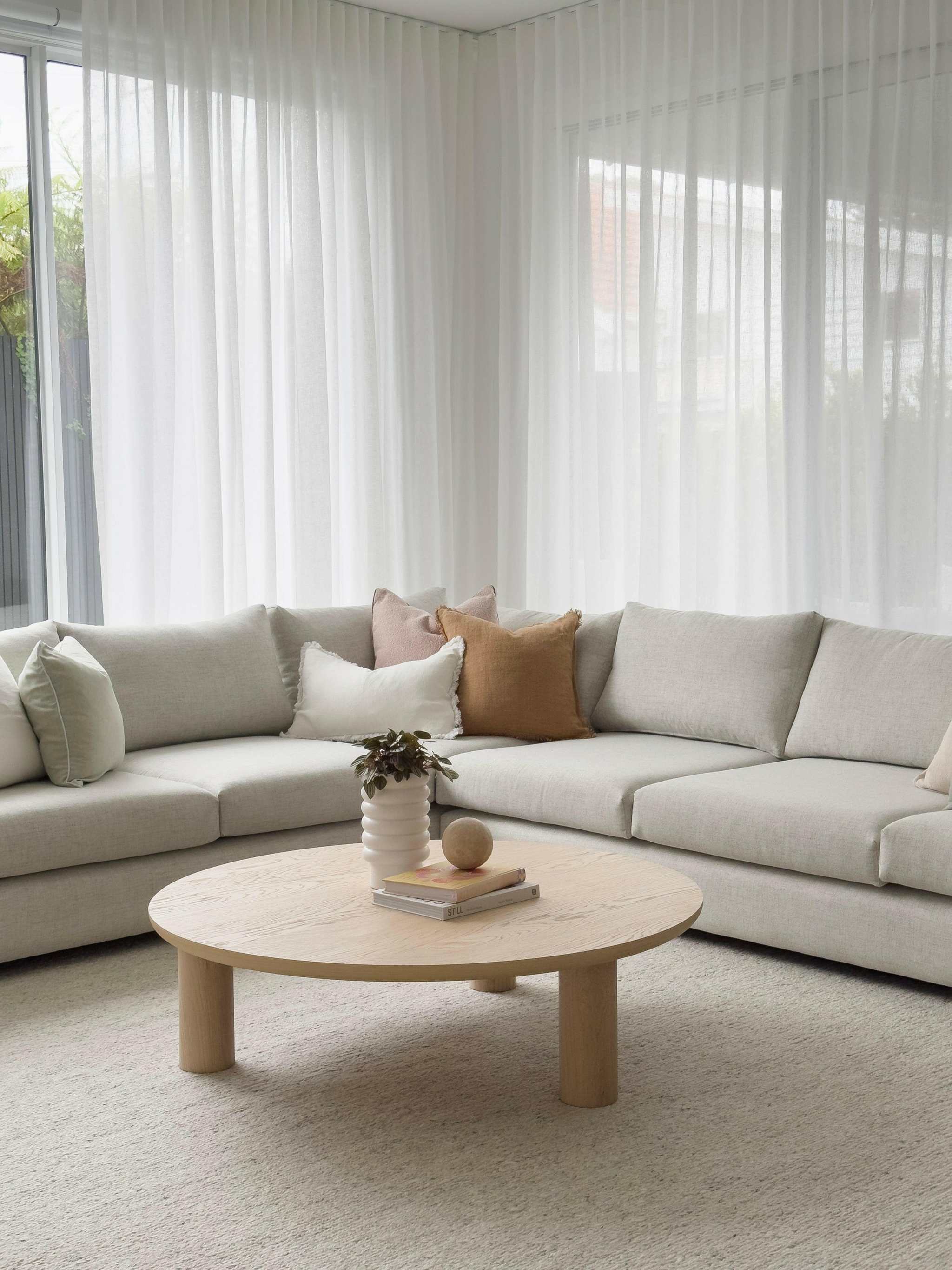 Light grey cushioned norsuHOME sofa in spacious living room with beige round wooden coffee table and neutral pillows