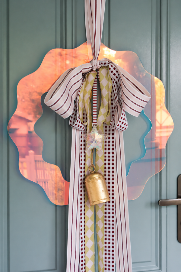norsu STUDIO 55cm iridescent perspex Christmas wreath with a hand-tied striped and harlequin ribbon bow and brass bell, on a green front door