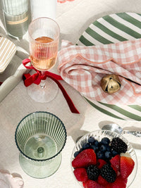 Set of four green Saltara RPET tumblers with ribbed texture, displayed on a table with a checkered cloth, plated berries, and striped dishware.