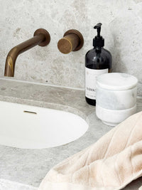 Stackable marble jewellery organiser canister on bathroom countertop with brass faucet and beige towel