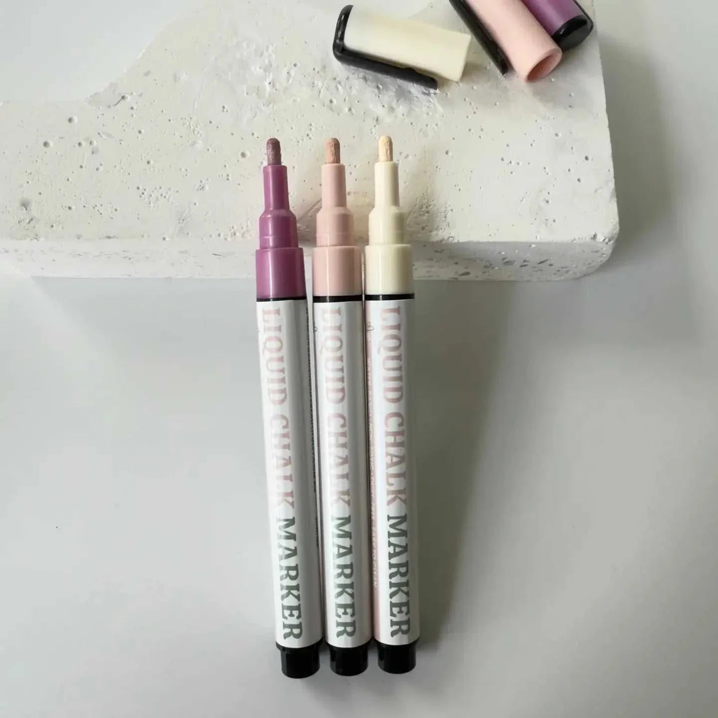 Set of three neutral color liquid chalk markers with fine reversible nibs on a concrete block background