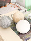CoTheory Orbit Sphere Table Sculpture in beige travertine displayed with other stone spheres on books