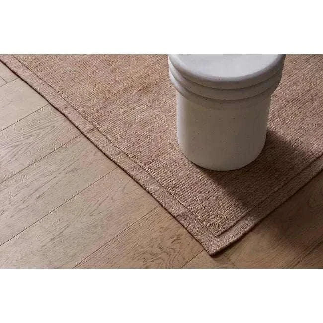 GlobeWest Bower Frame Rug in rose color, handwoven wool, displayed on wooden floor with ceramic vase.