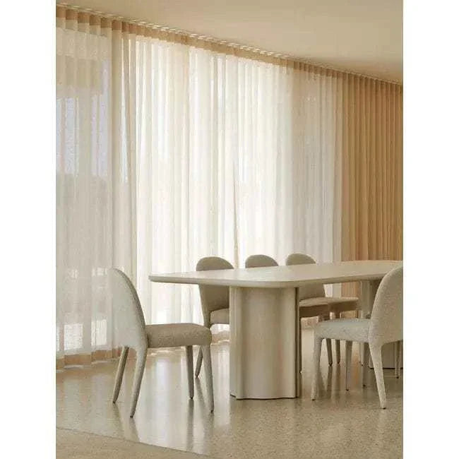 GlobeWest Leon Dining Table in porcelain finish with sculptural fluted pillar legs and rounded corners surrounded by modern beige chairs in a sunlit room