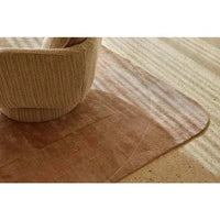 GlobeWest Tepih Curve Rug in dusty rose with subtle geometric pattern and rounded edges beneath a textured armchair