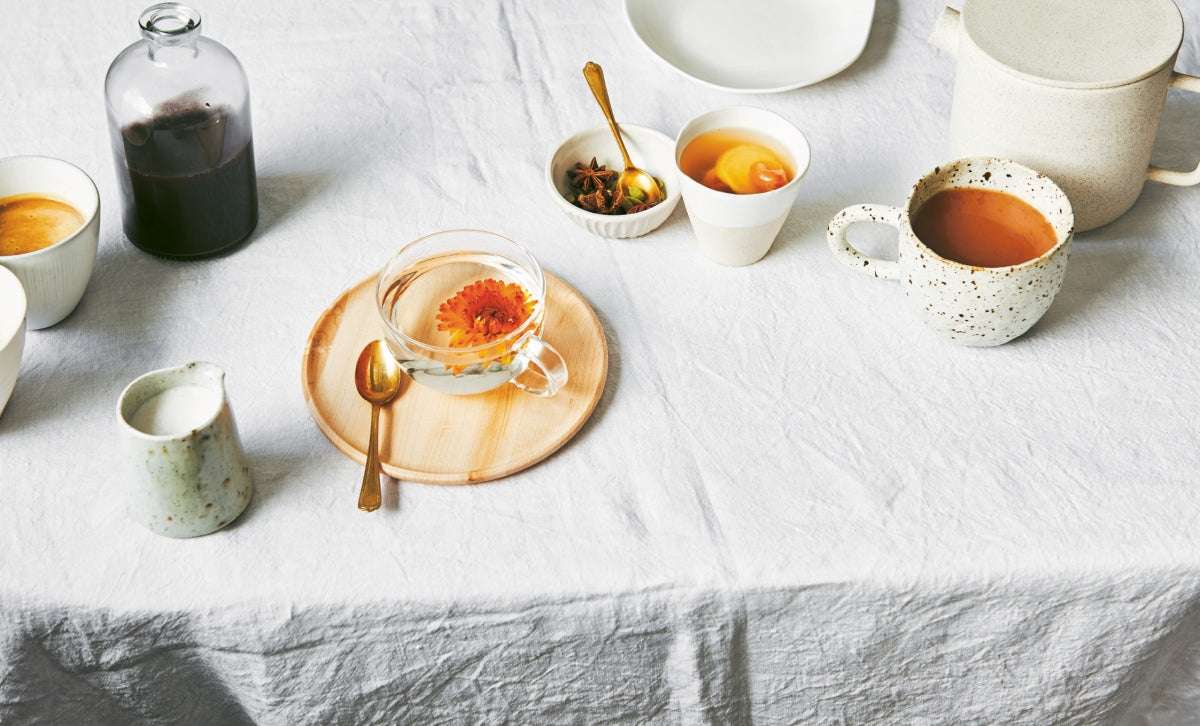 Minimalist tea set with cups, saucer, and spices on a white linen tablecloth for Gut Guide wellness program