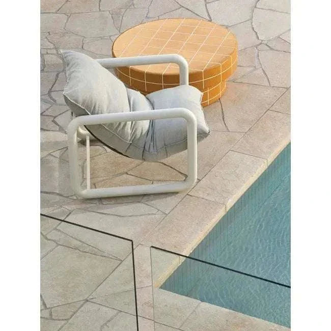 Round GlobeWest Seville Tile coffee table in pearl white beside modern white cushioned chair by poolside