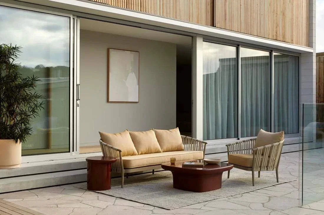Petra Sphere Side Table in burgundy glaze with glass-reinforced concrete base, placed outdoors beside beige cushioned seating.