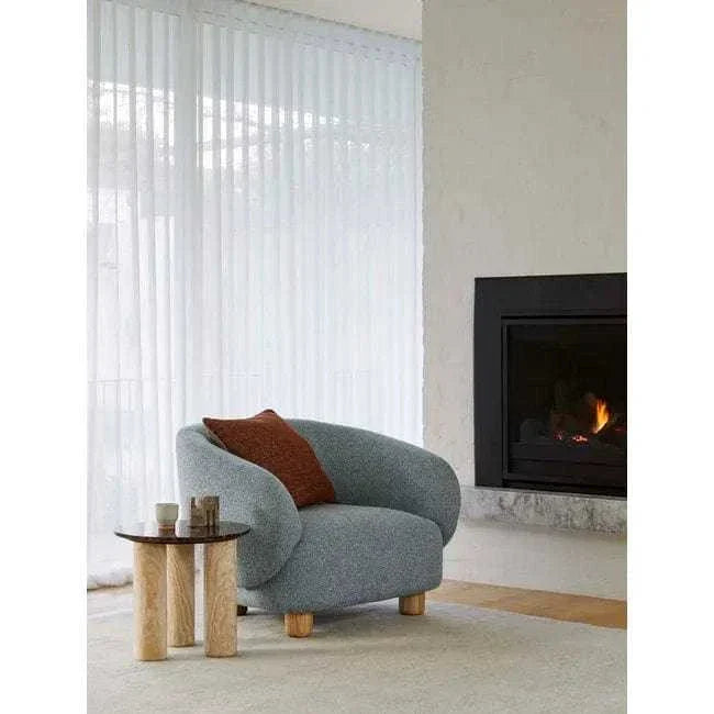 GlobeWest Flo Occasional Chair in Nimbus fabric with natural ash wooden legs beside small table and fireplace in modern living room