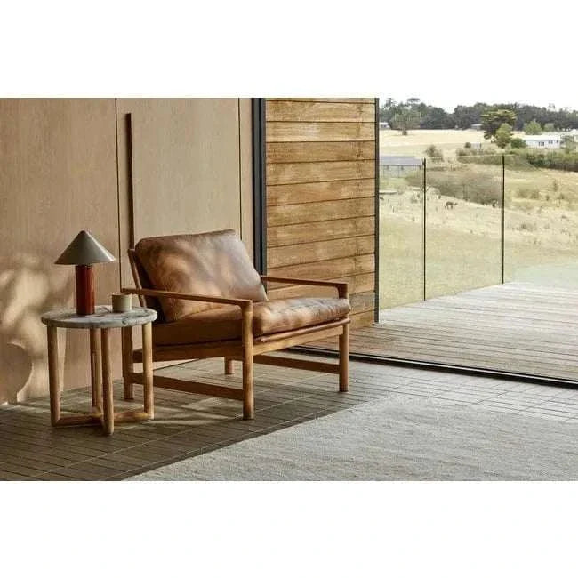 GlobeWest Pinnacle Table Lamp in russet with iron base and oyster grey shade on wooden side table next to leather armchair in modern living room with glass wall view