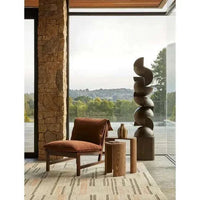 Modern interior setting with a ceramic Hanson Hako Vase in sepia stripe on a wooden side table next to a rust-colored lounge chair and natural stone wall