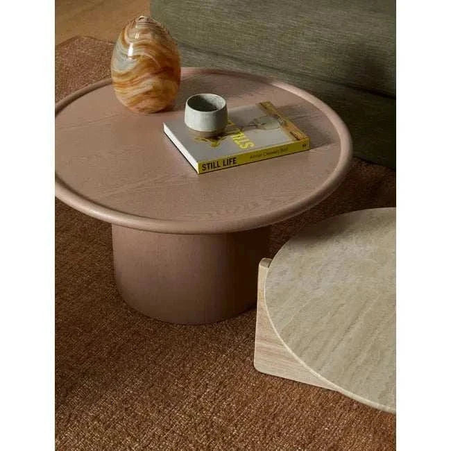 Pippa Coffee Table in chai tone with round ash veneer top and sculptural pedestal base on brown rug with decorative items.