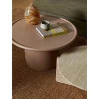 Pippa Coffee Table in chai tone with round ash veneer top and sculptural pedestal base on brown rug with decorative items.