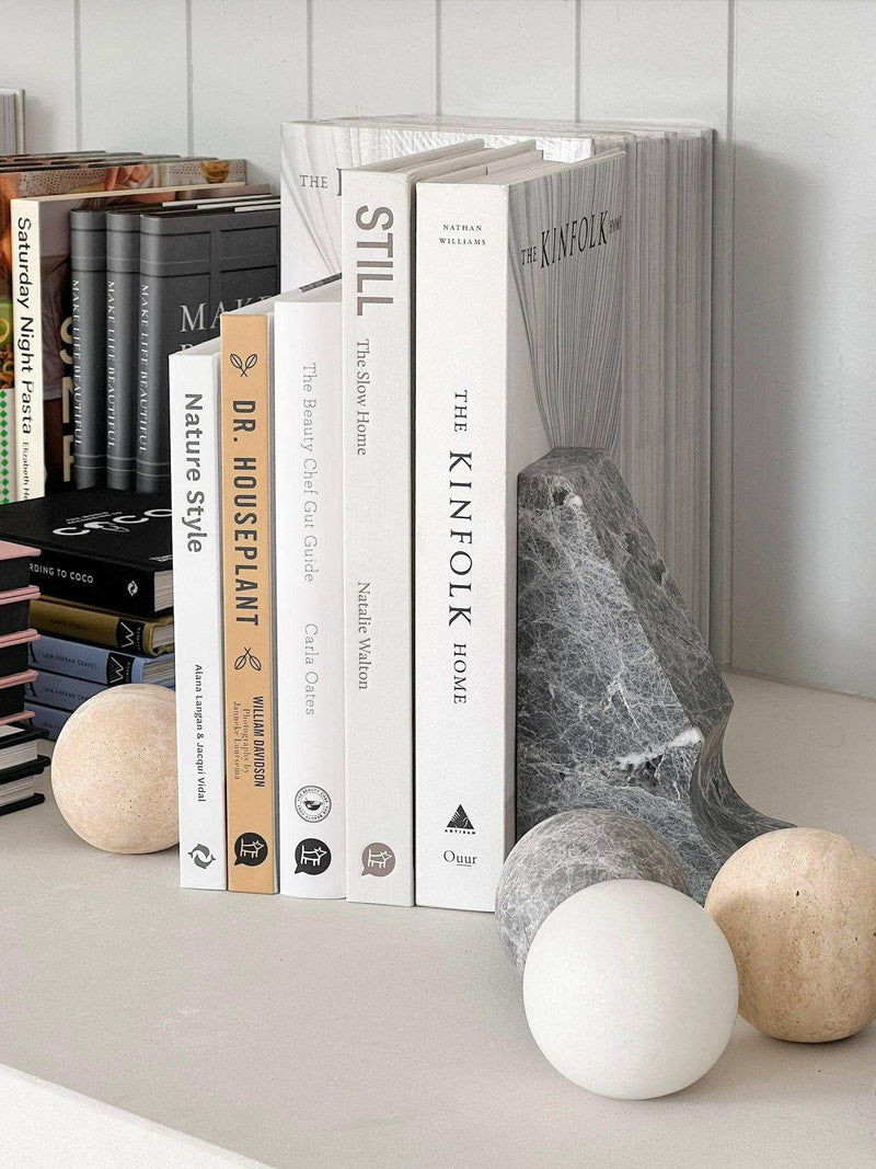 CoTheory Orbit Sphere Table Sculpture in beige travertine displayed with books and a grey stone bookend