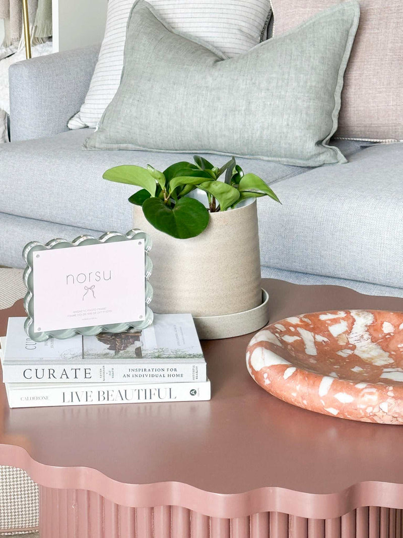 norsu Studio scalloped magnetic photo frame with acrylic background on pink scalloped table near green plant and books in modern living room