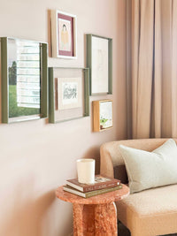 norsu STUDIO sage acrylic box gallery frame displaying various artworks on a beige wall above a cozy chair and side table
