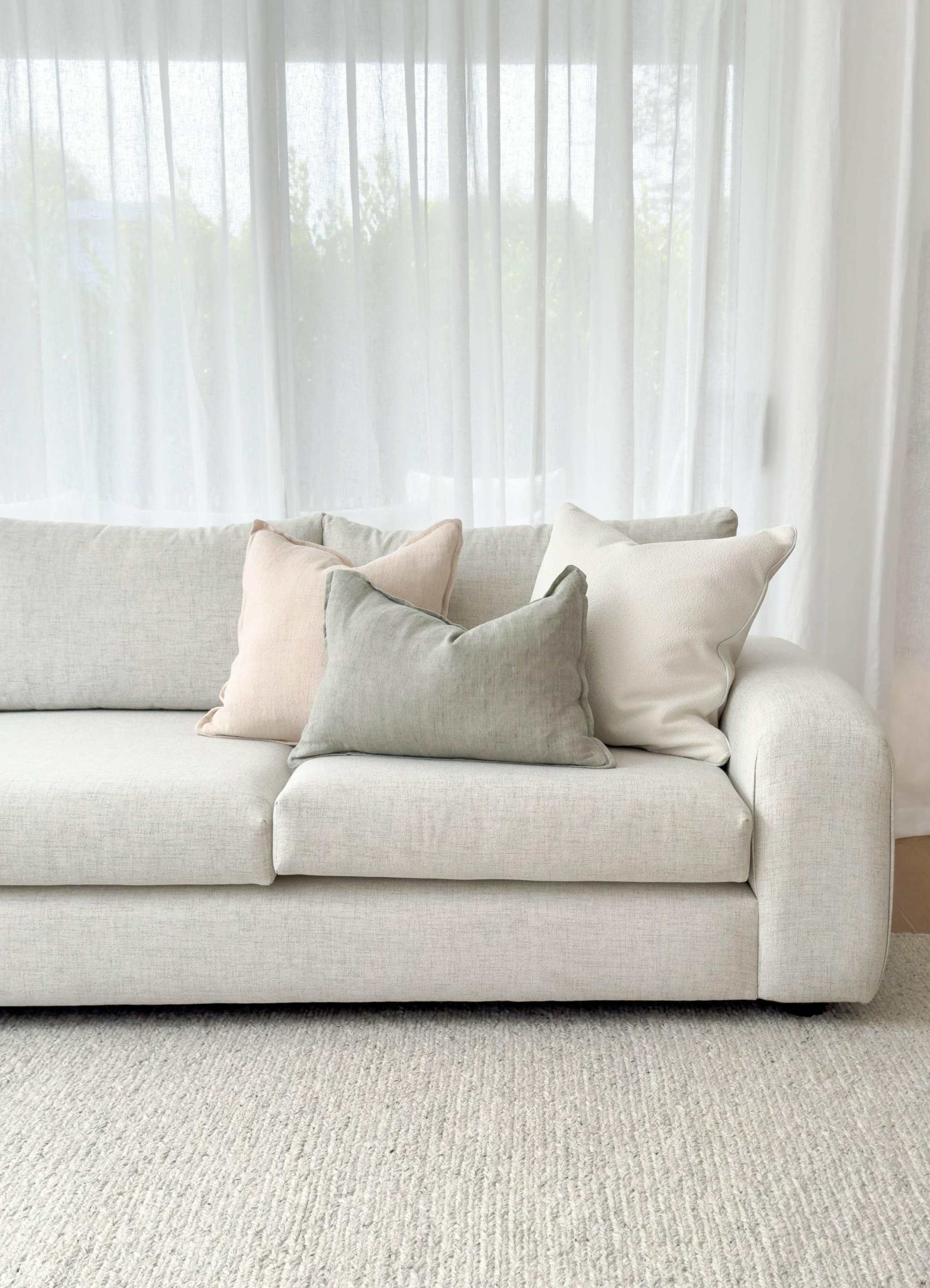 Minimalist light beige norsuHOME sofa with soft textured cushions in neutral tones against sheer white curtains.