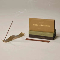 Gentle Habits Brass Wave Incense Holder with smooth wave design holding burning incense stick next to stacked incense boxes and extra sticks.