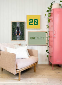 Modern living room with customizable wall art prints featuring a framed number 20 and "One Shot" text design next to a pink locker and beige sofa