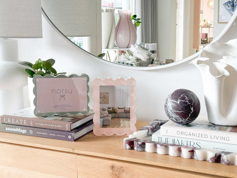norsu Studio scalloped magnetic photo frame in blush on wooden surface with decorative books and round mirror background