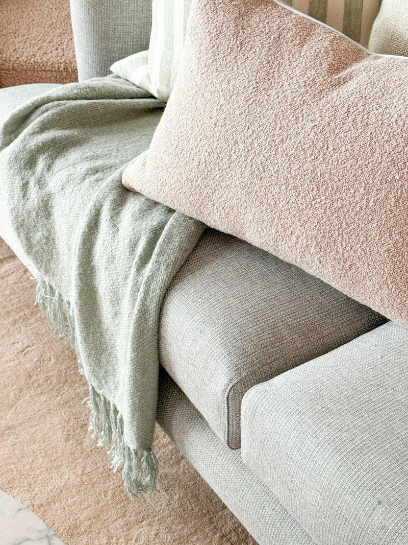 norsu Studio Cushion blush boucle with white leather piping on grey sofa with green throw blanket
