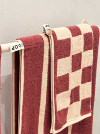 Loop Home Hand Towel in Ruby and Almond Blush with checkerboard jacquard weave hanging on a rack