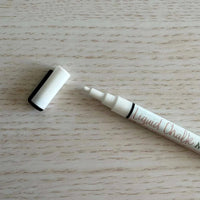 White liquid chalk marker with fine bullet tip and removable cap on wooden surface
