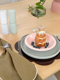 Pink norsu Studio Bow Bowl with deep pink bow design holding dessert on layered plates on wooden table setting