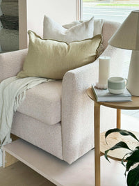 Blush boucle norsu Studio Swivel Chair with feather-filled cushion in a cozy living space next to a wooden side table and lamp