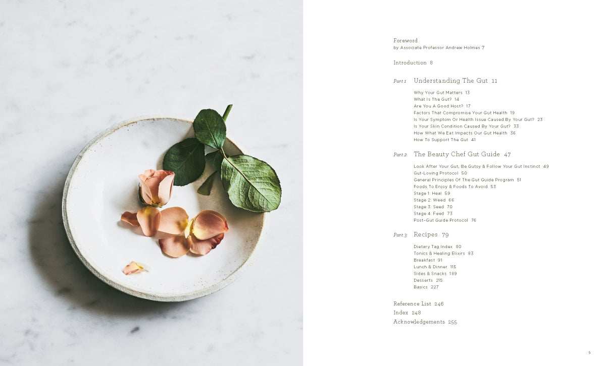 The Beauty Chef Gut Guide book page with table of contents and a plate with rose petals and green leaves on a marble surface