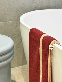 Loop Home Hand Towel in ruby and almond blush pinstripe hanging on bathtub edge in modern bathroom