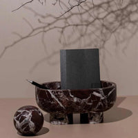 CoTheory Orbit Table Sculpture Rosso Levanto marble sphere beside matching marble bowl with black notebook and pen