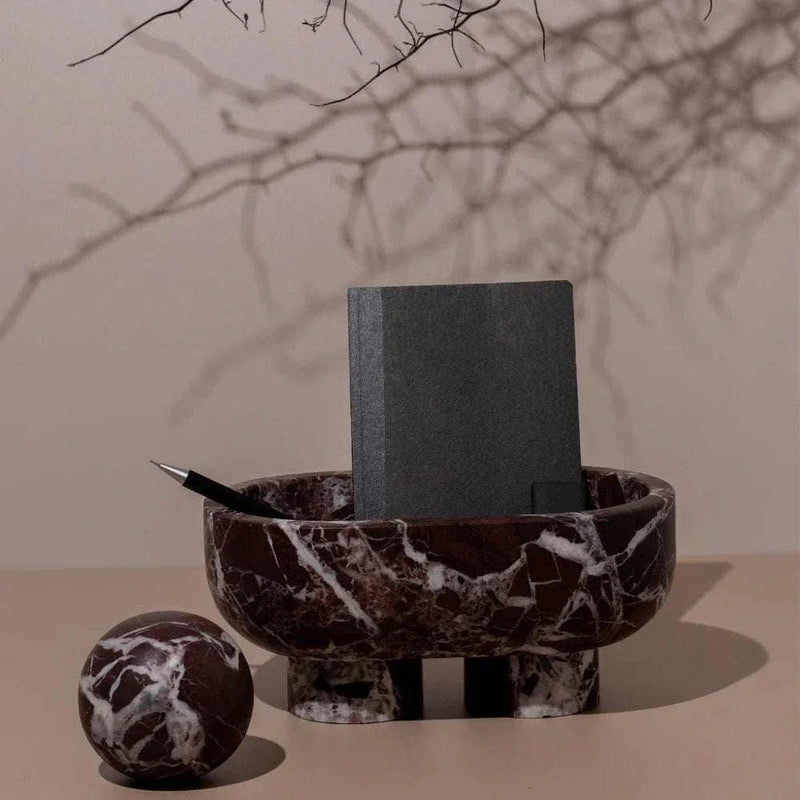 CoTheory Orbit Table Sculpture Rosso Levanto marble sphere beside matching marble bowl with black notebook and pen