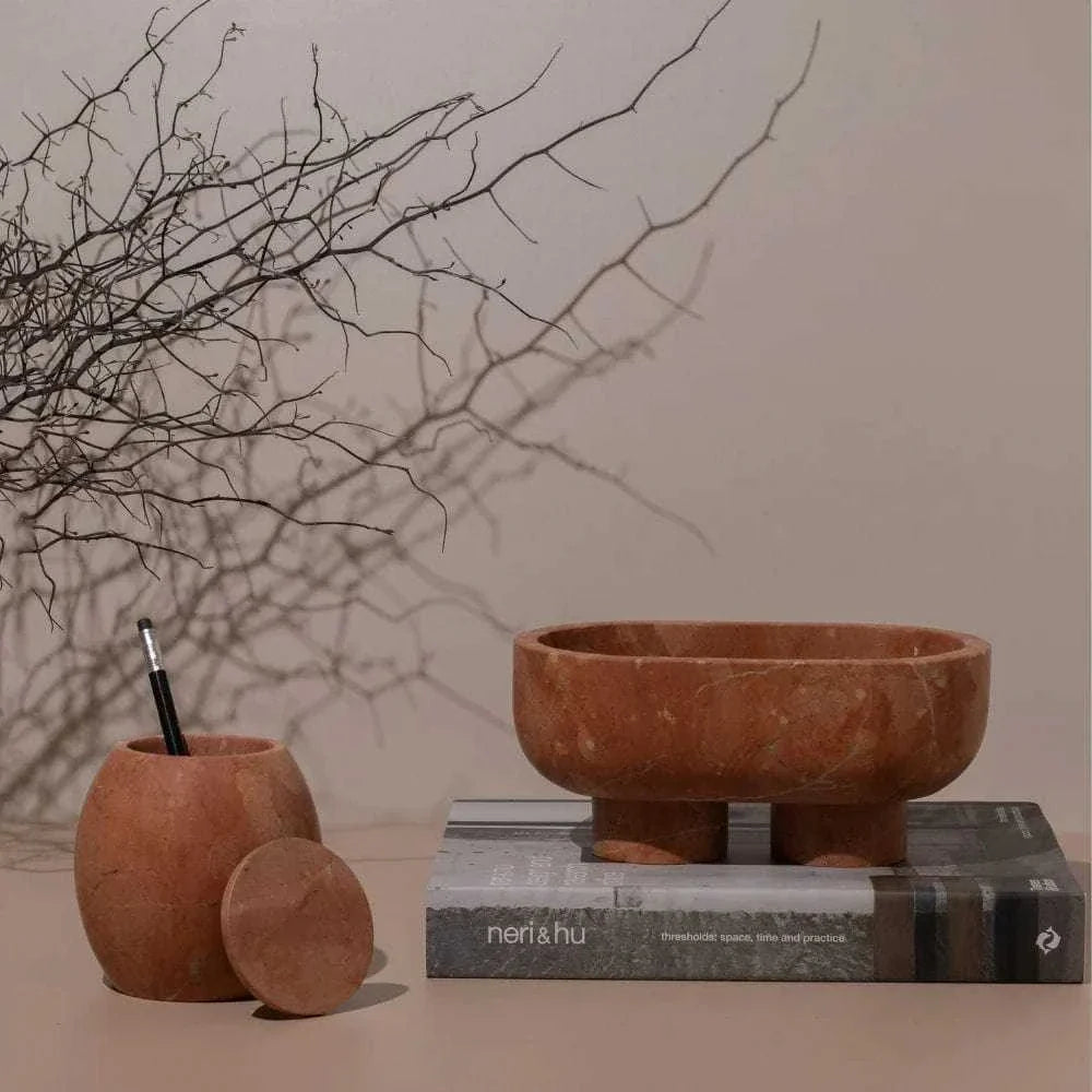 CoTheory Marble Footed Oval Tray Rosso Alicante on book with decorative wooden container and dried branches background