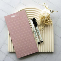 Blush pink reusable fridge shopping and to-do list with white marker pens and decorative dried flowers on a textured white tray