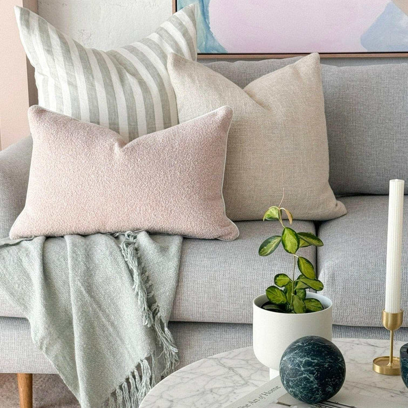 norsu Studio Cushion in blush boucle with white leather piping on a grey sofa with neutral pillows and throw blanket
